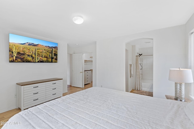 bedroom featuring arched walkways, light wood finished floors, a walk in closet, and connected bathroom