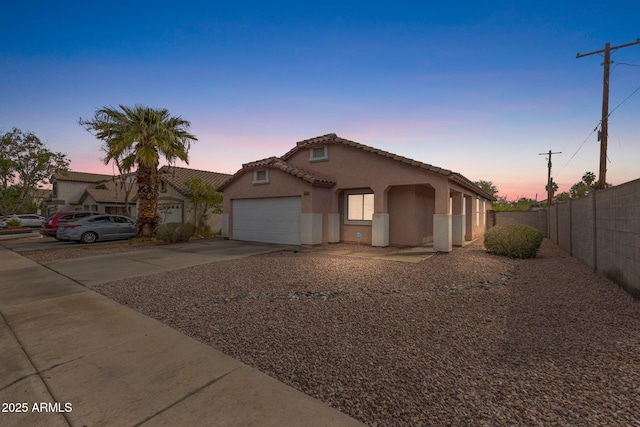 view of front of home featuring stucco siding, driveway, a tile roof, fence, and an attached garage