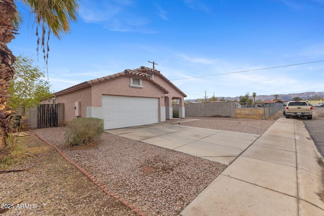 view of side of home featuring a tiled roof, stucco siding, fence, an attached garage, and driveway