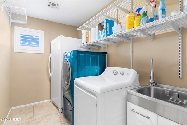 clothes washing area with sink, light tile patterned floors, and washing machine and clothes dryer