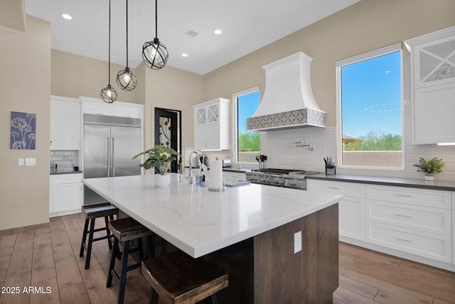 29067 N 71st Ave, Peoria, AZ 85383 - kitchen featuring premium range hood, stainless steel built in fridge, backsplash, an island with sink, and light wood-style flooring