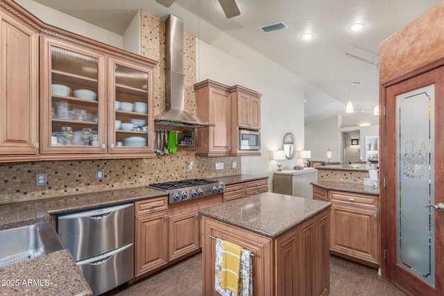 kitchen with appliances with stainless steel finishes, wall chimney exhaust hood, a kitchen island, decorative light fixtures, and decorative backsplash