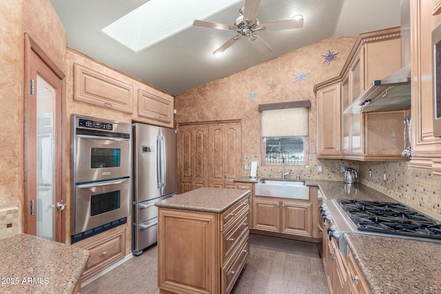 kitchen with appliances with stainless steel finishes, sink, vaulted ceiling with skylight, light brown cabinetry, and a center island