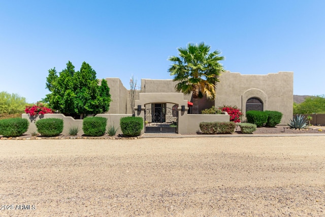 pueblo-style house with a fenced front yard, a gate, and stucco siding