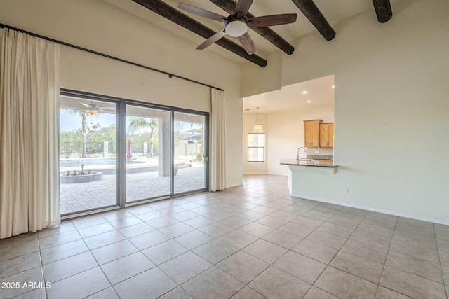 empty room featuring light tile patterned floors, baseboards, beamed ceiling, a high ceiling, and a sink