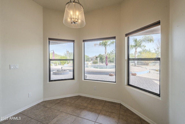 tiled spare room featuring baseboards and a chandelier