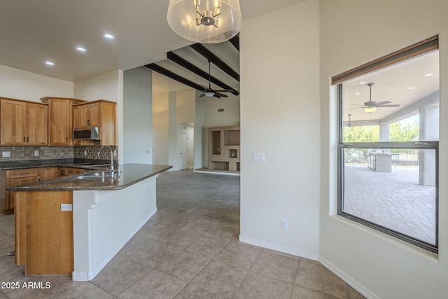 kitchen with a peninsula, baseboards, backsplash, brown cabinetry, and stainless steel microwave