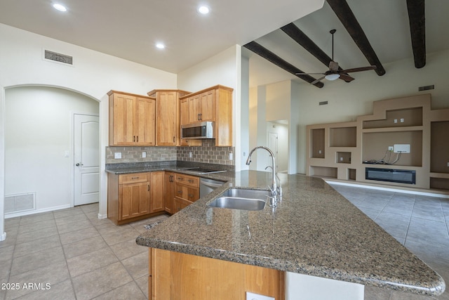 kitchen featuring stainless steel appliances, a sink, visible vents, tasteful backsplash, and dark stone countertops