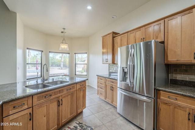 kitchen featuring light tile patterned floors, stainless steel fridge, tasteful backsplash, brown cabinetry, and a sink