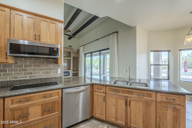 kitchen featuring a wealth of natural light, backsplash, appliances with stainless steel finishes, a sink, and dark stone countertops