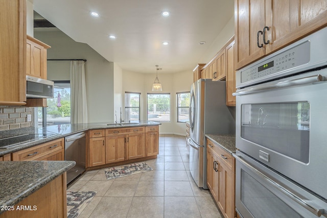 kitchen featuring light tile patterned floors, a peninsula, a sink, appliances with stainless steel finishes, and backsplash