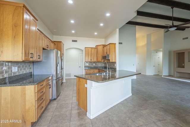 kitchen with arched walkways, stainless steel appliances, a sink, dark stone countertops, and a peninsula