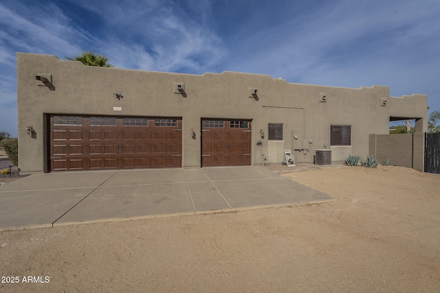 pueblo revival-style home with a garage, concrete driveway, cooling unit, and stucco siding