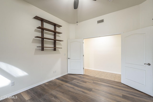 spare room with a ceiling fan, visible vents, baseboards, and wood finished floors