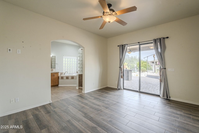 spare room featuring arched walkways, baseboards, and wood finished floors