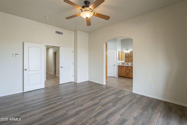 unfurnished bedroom featuring baseboards, visible vents, arched walkways, and dark wood-type flooring