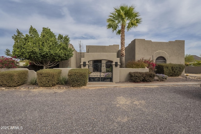 pueblo-style house with a fenced front yard, a gate, and stucco siding