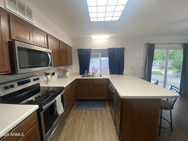 903 W Jacinto Cir, Mesa, AZ 85210 - kitchen with stainless steel appliances, a peninsula, light wood-style flooring, a breakfast bar area, and light countertops