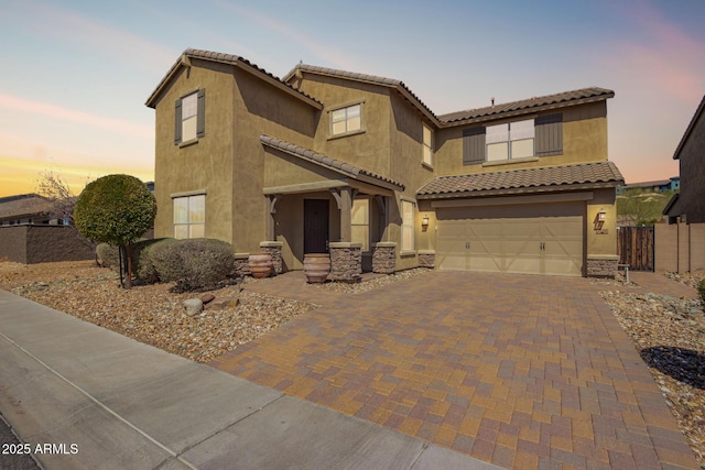 view of front facade featuring a tiled roof, decorative driveway, a garage, and stucco siding