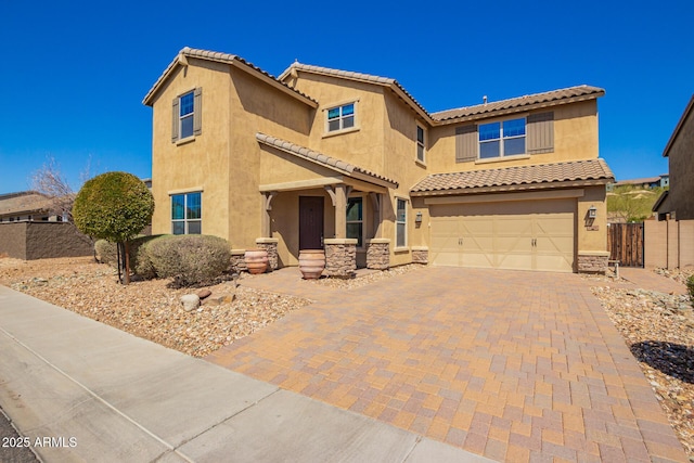 mediterranean / spanish house with stucco siding, decorative driveway, stone siding, fence, and an attached garage