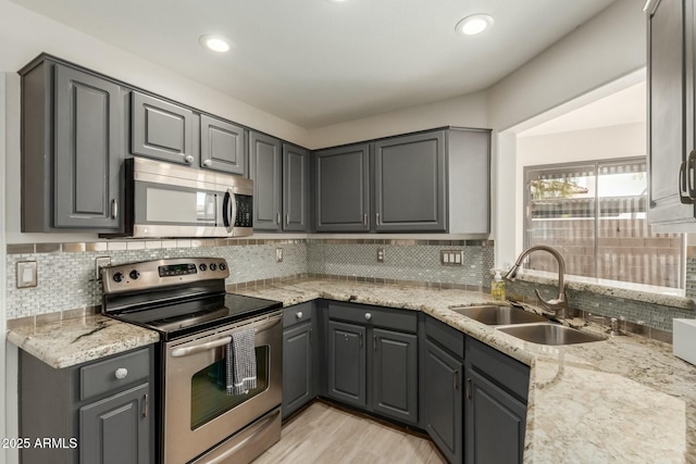 kitchen with light stone countertops, gray cabinetry, stainless steel appliances, and a sink