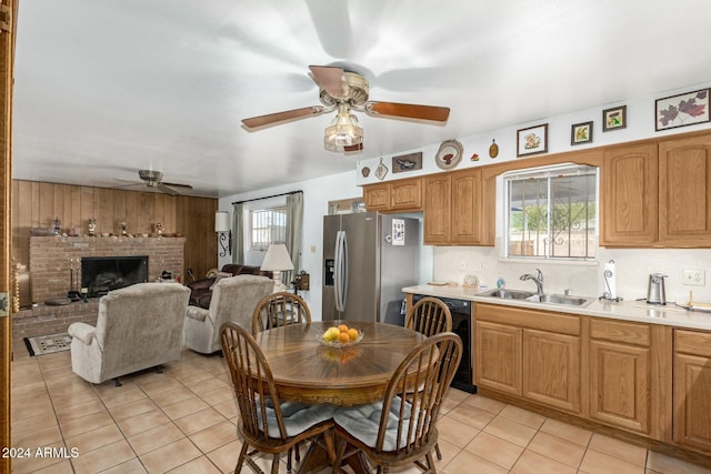 kitchen featuring dishwasher, sink, a brick fireplace, stainless steel refrigerator with ice dispenser, and light tile patterned floors