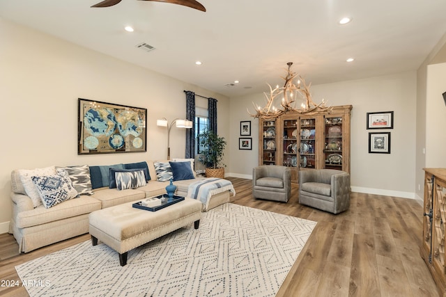 living room featuring ceiling fan with notable chandelier and light wood-type flooring