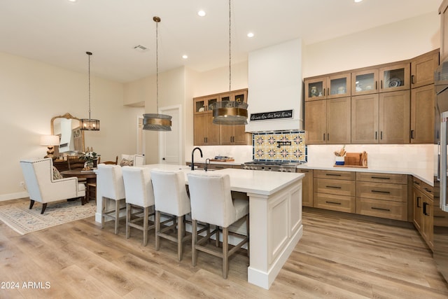 kitchen with premium range hood, a breakfast bar, light wood-type flooring, a kitchen island with sink, and decorative backsplash