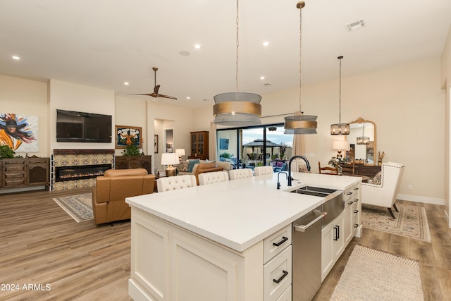 kitchen with sink, light wood-type flooring, pendant lighting, a kitchen island with sink, and white cabinets