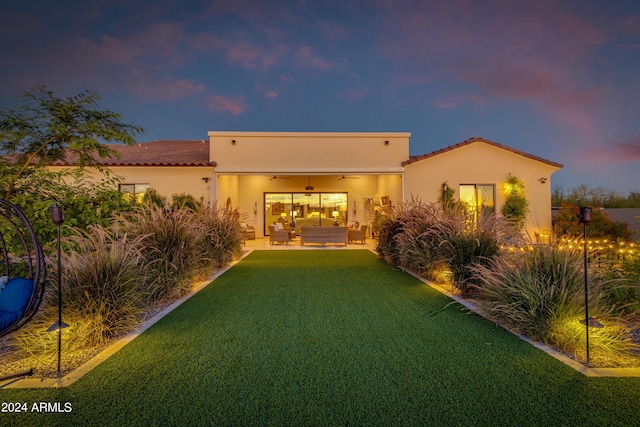 back house at dusk featuring a yard, outdoor lounge area, a patio, and ceiling fan