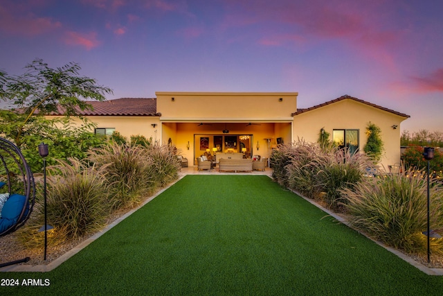 back house at dusk featuring a yard, an outdoor hangout area, ceiling fan, and a patio area