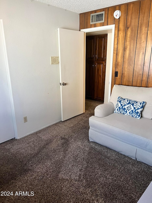 unfurnished living room with dark carpet, wooden walls, and a textured ceiling