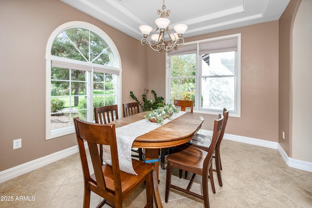 dining space with a tray ceiling, arched walkways, an inviting chandelier, light tile patterned floors, and baseboards