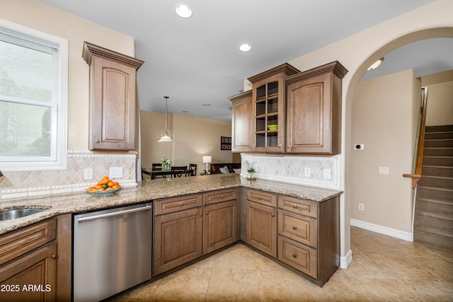 kitchen with arched walkways, light stone countertops, glass insert cabinets, and stainless steel dishwasher