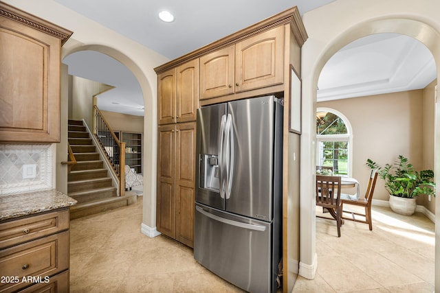 kitchen featuring light tile patterned floors, light stone countertops, baseboards, stainless steel fridge, and tasteful backsplash