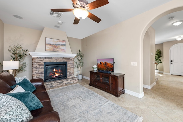 living room with light tile patterned floors, visible vents, baseboards, a fireplace, and arched walkways