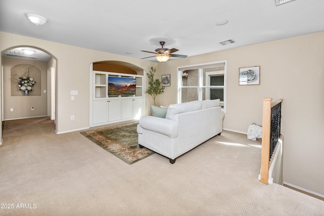 carpeted living area featuring built in shelves, a ceiling fan, visible vents, baseboards, and arched walkways