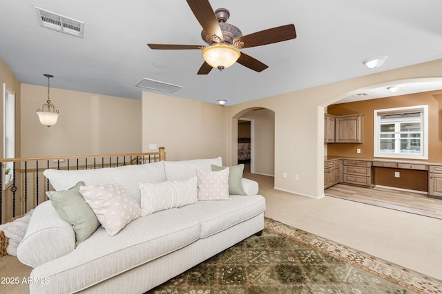 living room featuring a ceiling fan, light colored carpet, visible vents, and built in desk