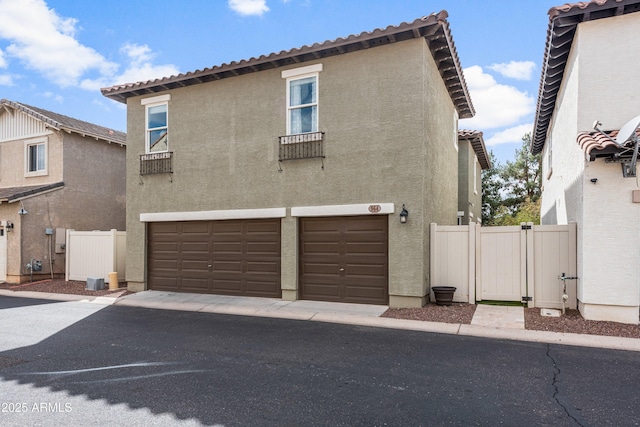 exterior space featuring stucco siding, a gate, fence, an attached garage, and a tiled roof