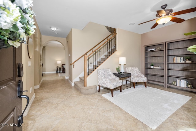 foyer entrance featuring stairs, baseboards, arched walkways, and a ceiling fan