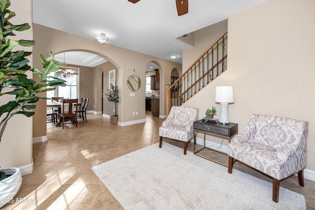 living area with stairway, ceiling fan with notable chandelier, baseboards, and arched walkways