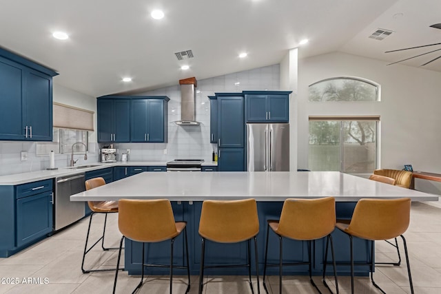 kitchen featuring blue cabinetry, wall chimney exhaust hood, visible vents, and stainless steel appliances