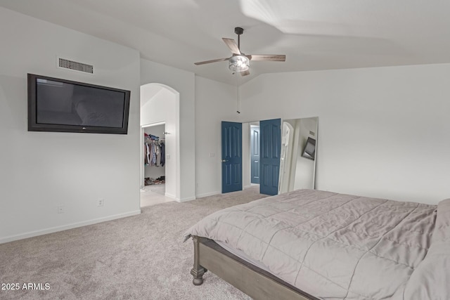 carpeted bedroom featuring a walk in closet, arched walkways, a closet, visible vents, and vaulted ceiling