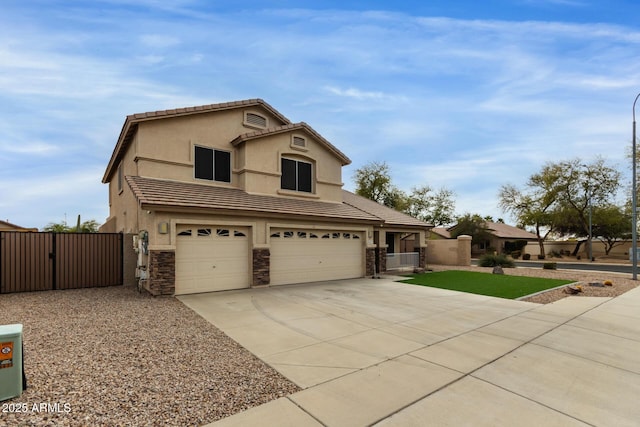 traditional-style home featuring concrete driveway, stone siding, a tile roof, a gate, and stucco siding