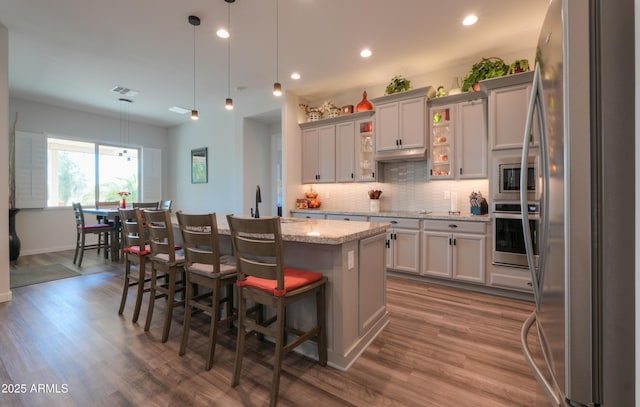 kitchen with stainless steel appliances, a kitchen island with sink, decorative light fixtures, and a kitchen bar