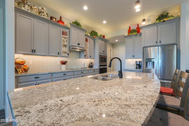 kitchen with stainless steel appliances, a center island with sink, light stone counters, and a breakfast bar area