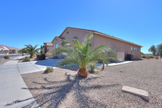 view of side of property featuring a tile roof, central AC, and stucco siding