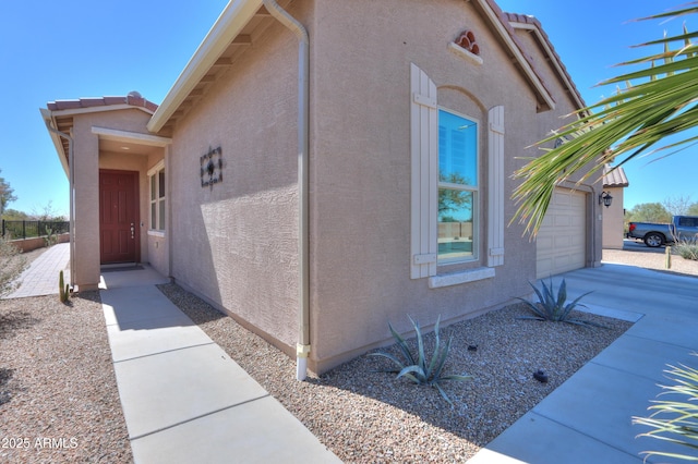 view of home's exterior with driveway, a tile roof, an attached garage, and stucco siding