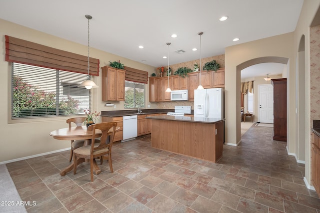 kitchen featuring a sink, a center island, white appliances, arched walkways, and baseboards