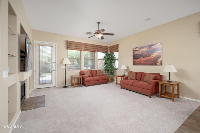 living area featuring baseboards, a ceiling fan, carpet flooring, and a tile fireplace